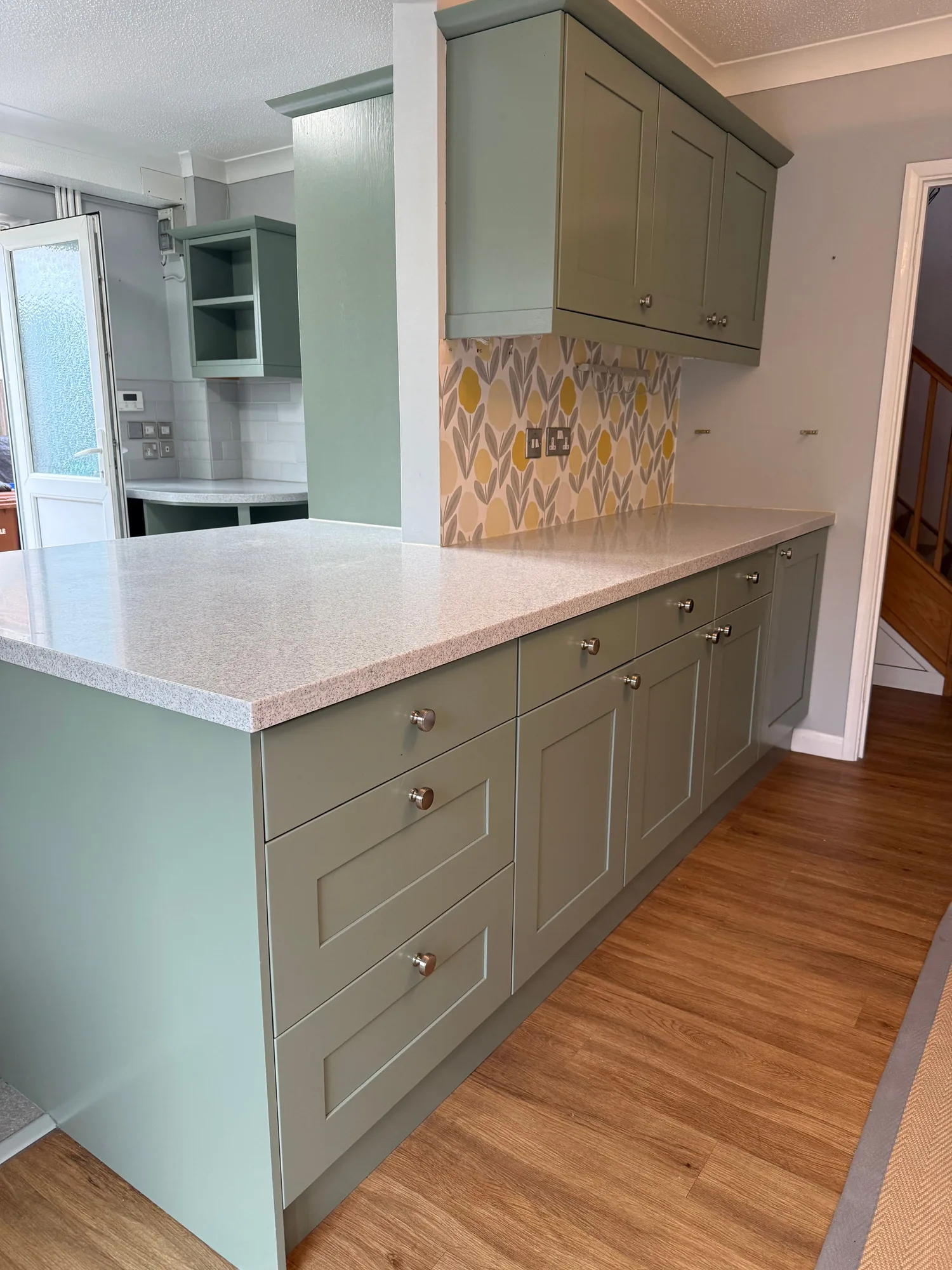 Sage green units with a white worktop and tiled splashback