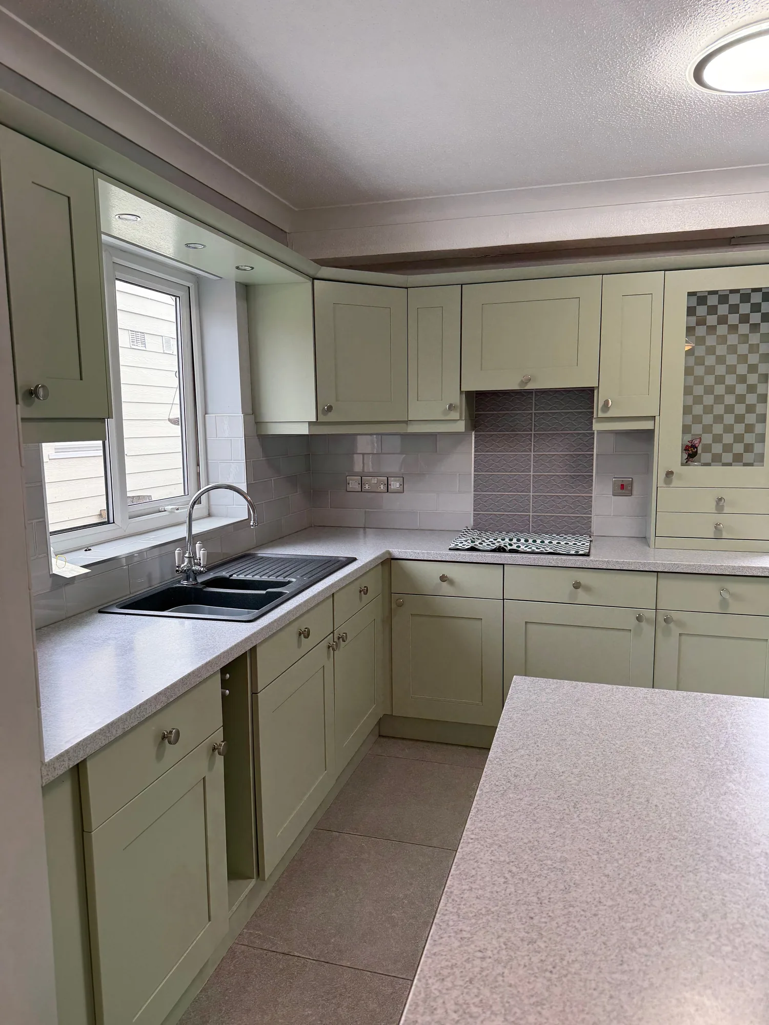 Olive green kitchen with a light worktop and window above the sink