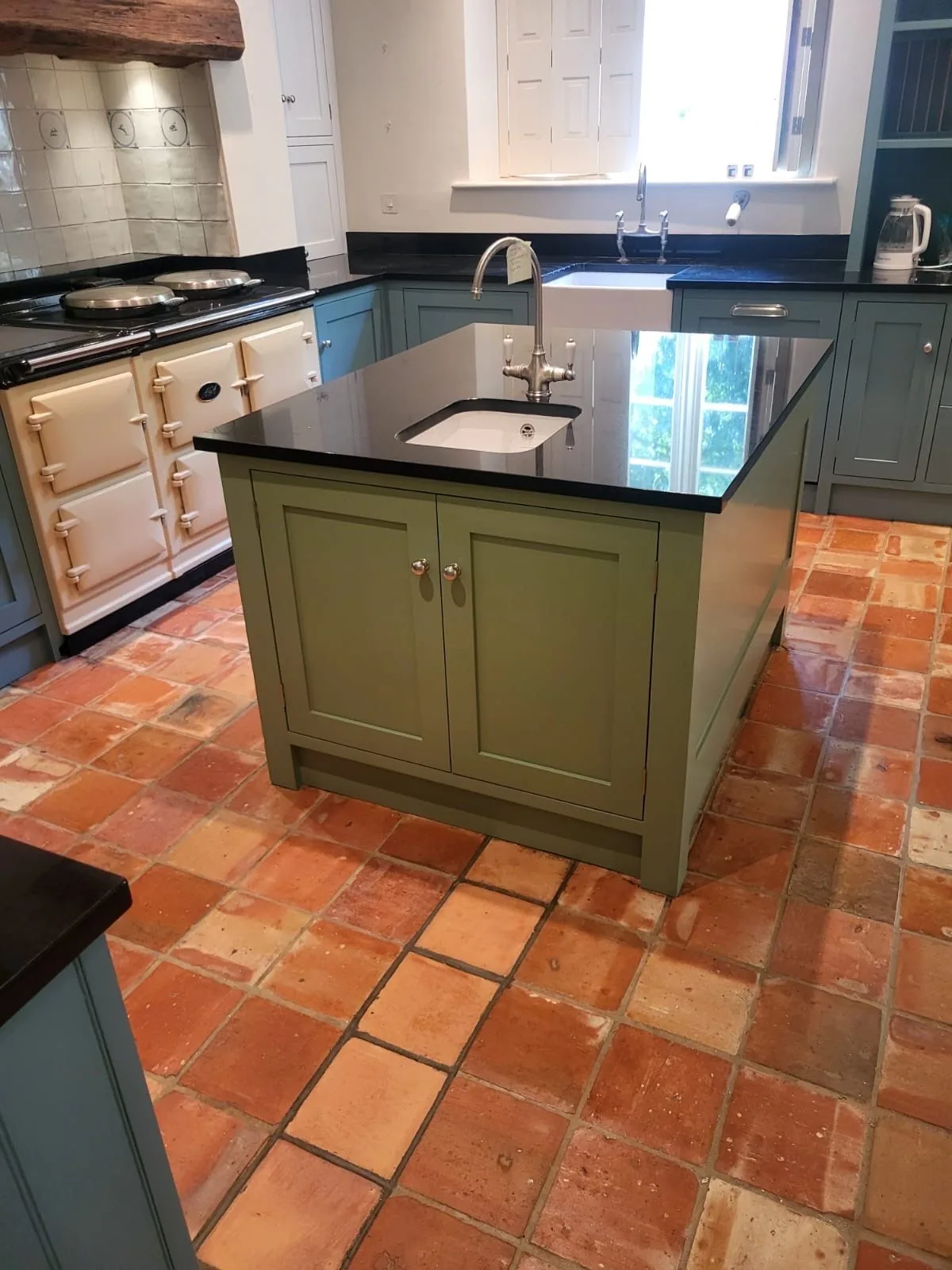 Olive green island with granite worktop over a terracotta floor